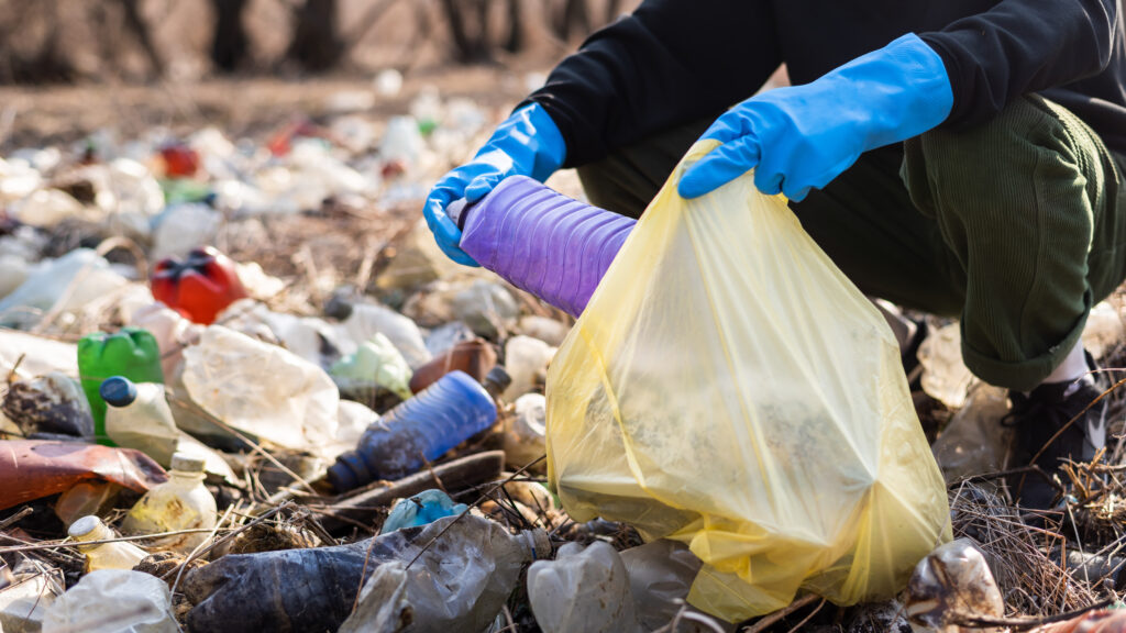 Man in gloves collecting scattered plastic bottles from the ground in the nature
