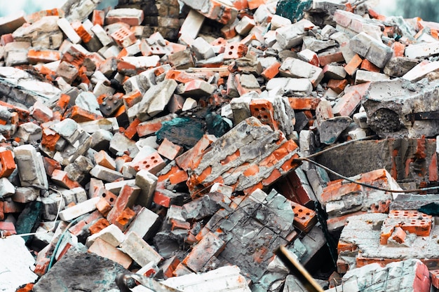 A close-up of a large pile of rubble, dominated by broken orange bricks and gray concrete chunks, haphazardly stacked across the frame. Several bricks show their characteristic holes, and a dark, rusted rebar protrudes from the lower right portion of the debris. The scene conveys demolition or structural collapse.
